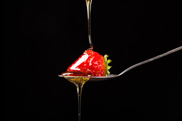 fresh strawberry on a spoon dipped in honey on black background