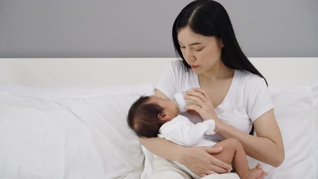 mother feeding milk bottle to her newborn baby on a bed

