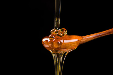 honey pouring into wooden spoon isolated on black background