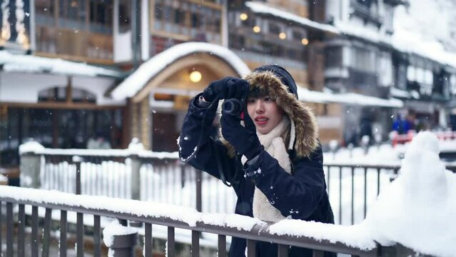 Asian woman tourist using digital camera taking picture during travel Ginzan onsen area in Yamagata prefecture, Japan in snow day. Attractive girl travel local village landmark on winter vacation.