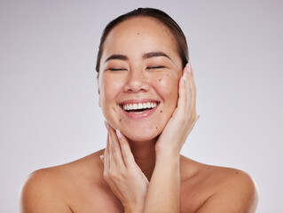 Skincare, hands on face and woman laughing in studio for cosmetics, dermatology and beauty glow. Happy aesthetic asian model person with makeup, skin mole and facial self care on grey background