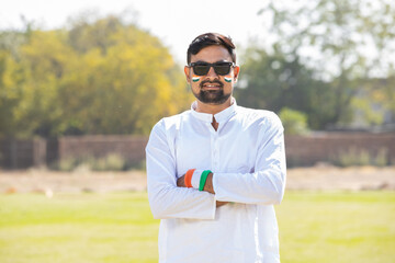 Portrait of young indian man wearing traditional white dress and sunglasses kurta and tricolor hand bands standing cross arms at park. celebrating Independence day or Republic day.