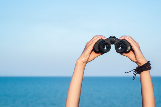 Female hands hold binoculars on the blue horizon, sky and sea background