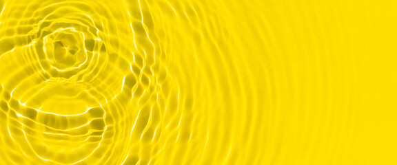 Drops fall on yellow water by sunlight. Top view, flat lay. Banner