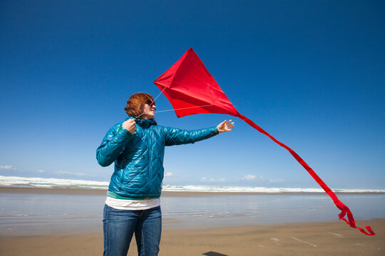 A young woman reaches for her red kite after flying it at a beach along the Oregon Coast