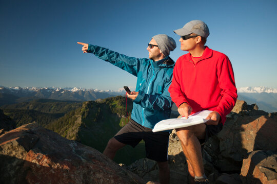 Two men use a paper map and a compass to identify nearby peaks while hiking in the backcountry.
