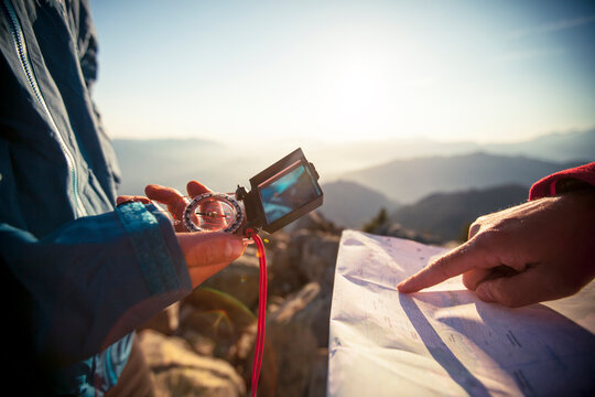 Two men use a paper map and a compass to navigate while hiking in the North Cascade Mountain Range.