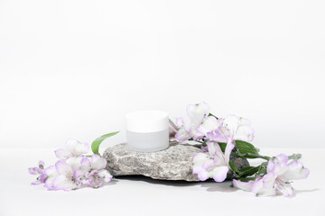 Obraz na płótnie Canvas A mock up white jar of cream on a natural stone podium pedestal, on a white table, with plant, flowers, with hard shadows. Stylish look of the product, identity.