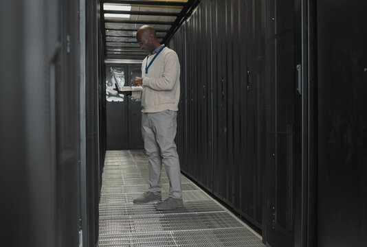 Server room, data center or IT black man with laptop for research, engineer working in dark server room. Computer, cybersecurity and analytics with male programmer problem solving or troubleshooting