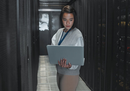 Woman with laptop, server room and IT, engineer and datacenter with software update and programming. Tech industry, cybersecurity and network with Asian female setting up firewall and database