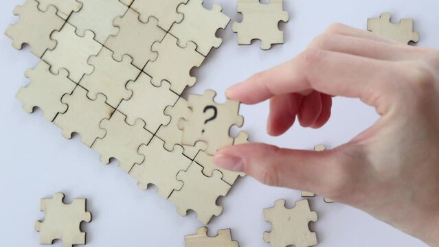 Woman's hand holds a wooden puzzle with a question mark against a background of empty puzzles. The concept of problem solving.