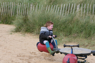 Red head boy wearing a coat having fun on a seesaw in a Playpark on a beach by an Ocean