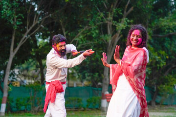 Obraz premium Indian man spraying color with water gun on woman at park. Holi festival concept.