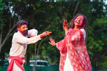 Indian man spraying color with water gun on woman at park. Holi festival concept.