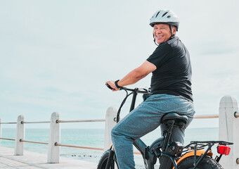 Electric bike, portrait or travel with a senior man on a promenade, riding eco friendly transport by the beach. Sustainability, cycling or mock up with a mature male tourist by the seaside for a ride