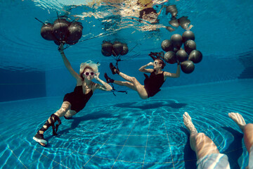 Underwater shoot of flying two women with black balloons - obrazy, fototapety, plakaty