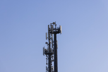 Telecommunications tower with cellular antennas and repeaters against a clear blue sky