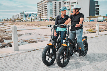 Fototapeta na wymiar Senior couple, electric bike and ride by the beach for fun bonding activity or travel together in the city. Happy elderly man and woman enjoying cruise on electrical bicycle for trip in Cape Town