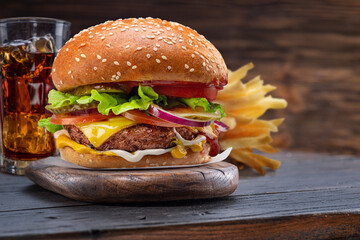 Tasty cheeseburger, glass of cola and french fries on wooden tray close-up.