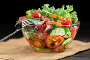 Vegetable salad with leafy greens in the glass oil is on the wooden table.