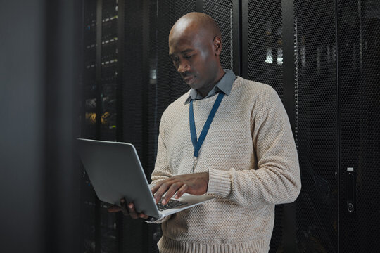 Laptop, server room and black man or technician in data center management, system or cybersecurity. Analysis, serious or power coding solution, engineering programmer or information technology person