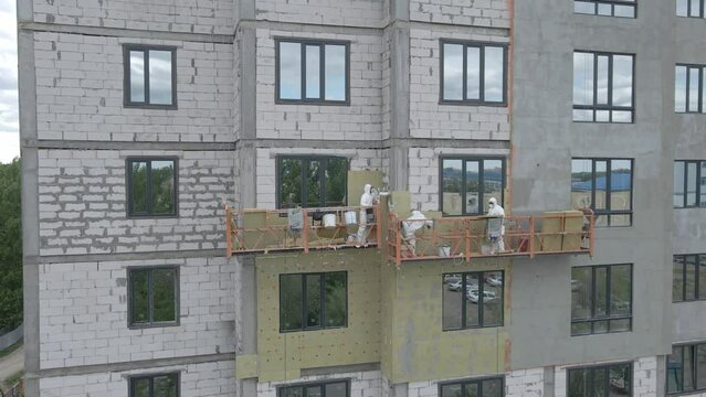Climbers on a suspended elevator paint the building. Industrial Painters Wall of Building Facade with White Paint using Paintbrush. Slow Motion. Thermal insulation. High quality 4k footage