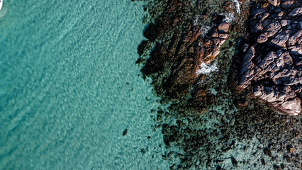 Drone photo of blue water surface with little rocks on the side. Aerial picture of shallow water in Dunsborough, South-west Australia. Ocean and rocks with small waves and foamy water.