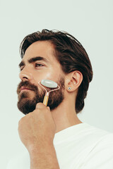 Jade roller for male skin: Young man massaging his face in a studio
