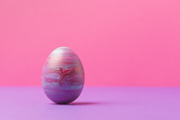 Decorative Easter egg painted in fluid art technique against pink background with copy space. Easter holiday greeting concept