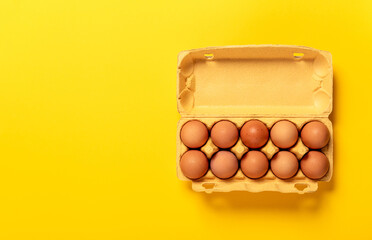 Ten chicken eggs in cardboard package isolated on yellow background. Top view, copy space. Big size XL. Concept of business card grocery store. Fresh eco farm product. Healthy organic food. Banner