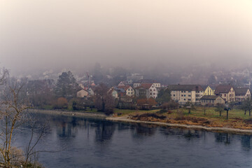 Fototapeta premium Aerial view of village Flurlingen with Rhine River in the foreground seen from railway station Neuhauen on a foggy winter day. Photo taken February 16th, 2023, Neuhausen, Switzerland.