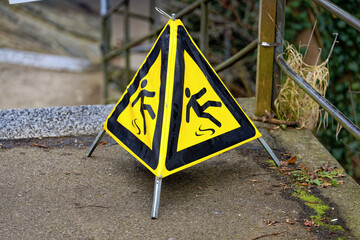 Yellow mobile triangle warning sign slippery floor at footpath at famous Rhine Falls on a foggy winter day. Photo taken February 16th, 2023, Laufen Uhwiesen, Switzerland.