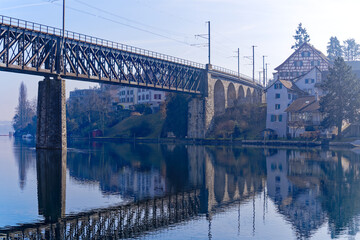 Scenic view of Rhine River at City of Schaffhausen with railway bridge and village of Feuerthalen in the background on a sunny winter day. Photo taken February 16th, 2023, Schaffhausen, Switzerland.