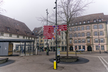 Square named Schifflände with red direction signs of bicycle tracks at City of Schaffhausen on a foggy winter day. Photo taken February 16th, 2023, Schaffhausen, Switzerland.