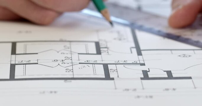 Close-up, an engineer calculates the values on a drawing of a house, takes notes and writes with a pencil in the background. Work with the drawing of the apartment, design.