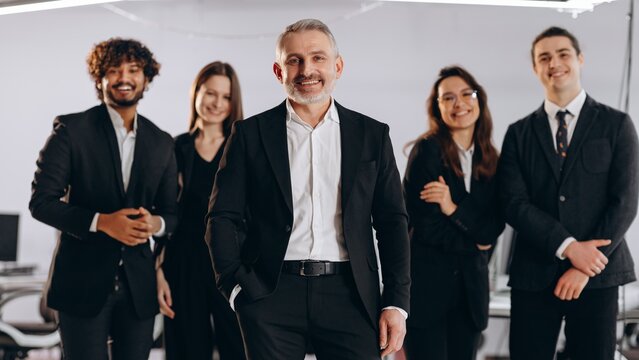 Smiling company executive with his team. Front view of laughing businesspeople in black suit posing together. Group of happy managers