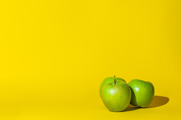 apples fruits ,three objects,hard shadow,green color round,lie on the surface of the yellow background.concept apples juice vitamins.