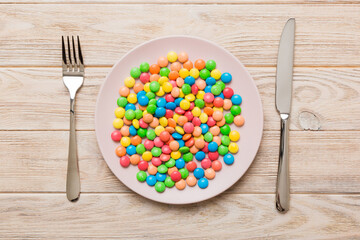 cutlery on table and sweet plate of candy. Health and obesity concept, top view on colored background