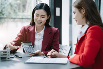 home loan officer uses a calculator with a house plan, a contract, signing an home buying agreement.