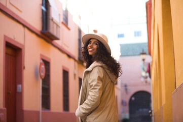 Obraz premium Young and beautiful Hispanic brunette woman with curly hair wearing a hat and coat for the cold walking in the city of seville while making different expressions and having fun.
