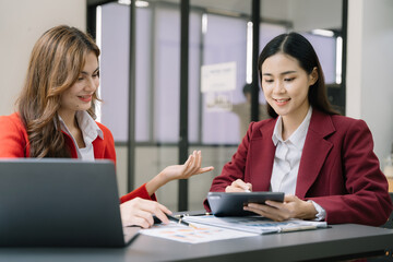 Fototapeta premium Asian women team brainstorming and discussing with financial data and report graph working search page on computer with new startup project. Idea presentation, analyze plans.