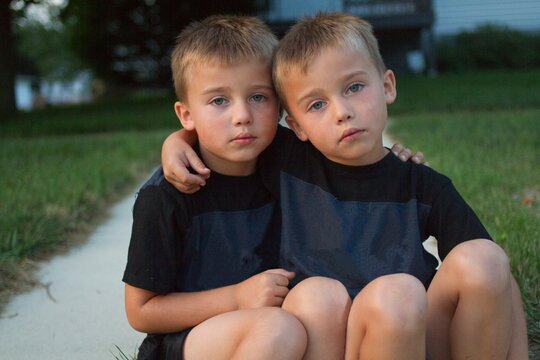 Portrait of twin brothers sitting on a street curb with their arms around each other, Lena, Illinois, USA