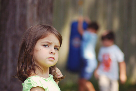 Portrait of an unhappy girl feeling left out with two boys playing in the background, USA