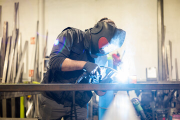 Profile view of a man working as a welder with a protective mask and work clothes performs a job...