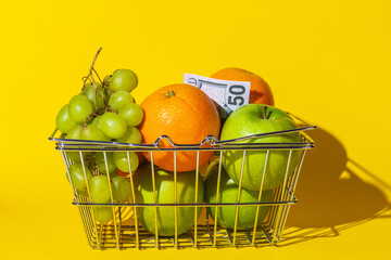 basket cart supermarket with fruit and dollar bill, fruit for food and money, multi-colored round paper, lie in a basket on the surface of the yellow background. concept Market basket