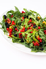 Summer delicious salad with arugula and fresh berries, red and black currants, sweet cherries and black mulberries, salad in an oval plate on a white background