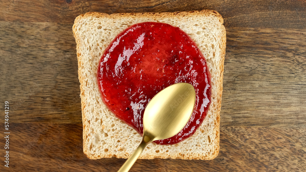 Wall mural Raspberry jam spreading on bread with a golden spoon, top view. Perfect traditional breakfast - Wall murals