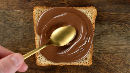 Сhocolate paste spreading on bread with a golden spoon, top view. Perfect traditional breakfast