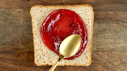 Raspberry jam spreading on bread with a golden spoon, top view. Perfect traditional breakfast