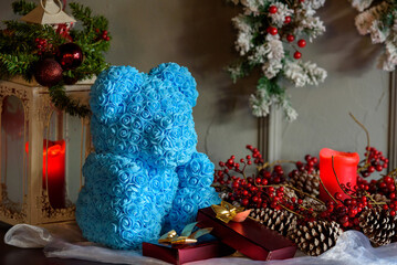 Close-up of a blue Teddy bear made of roses on a table next to assorted Christmas decorations